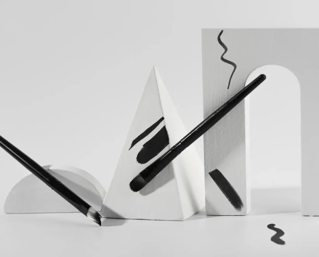 Visuel blanc avec crayon et pinceau noir représentant le secteur de la création graphique, domaine d'activité de l'entreprise Floki.