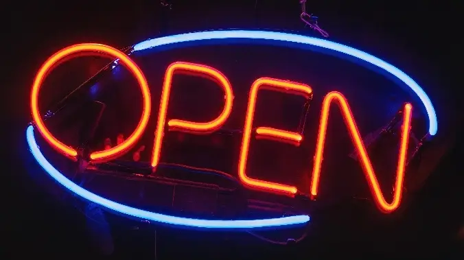 Enseigne néon lumineuse du mot "Open" représentant l'activité de l'agence de publicité Floki.
